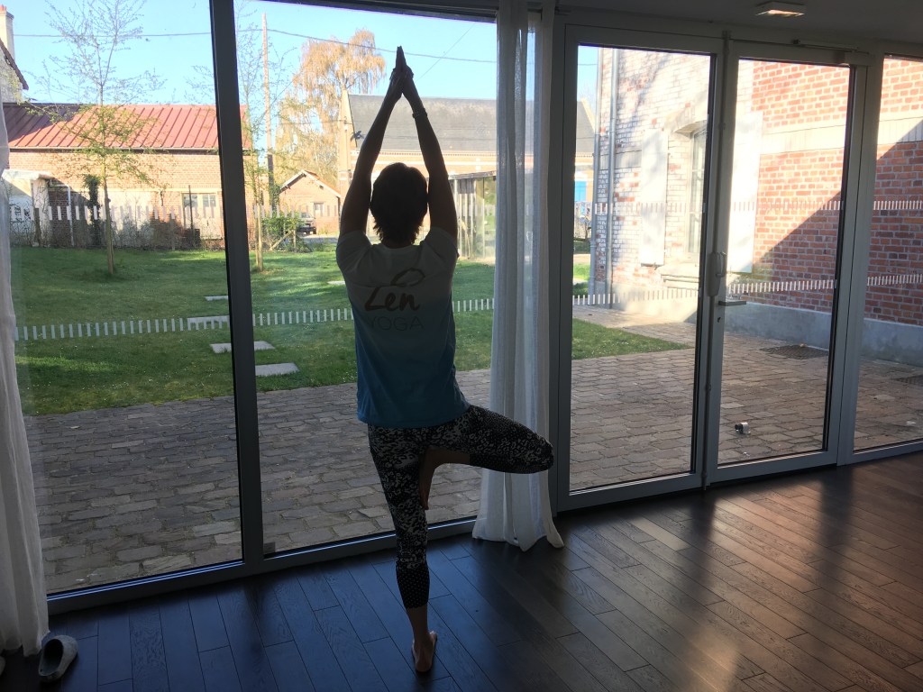 Annabel holding a Tree Vrkasana pose in front of some large windows